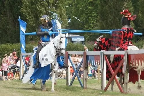 Two armoured knights on horseback clash at the tilt, a lance shattering against a shield